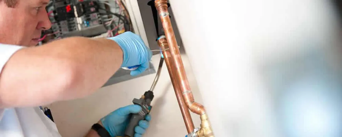 Water heater repair technician testing copper pipe connections and controls in Reading, MA
